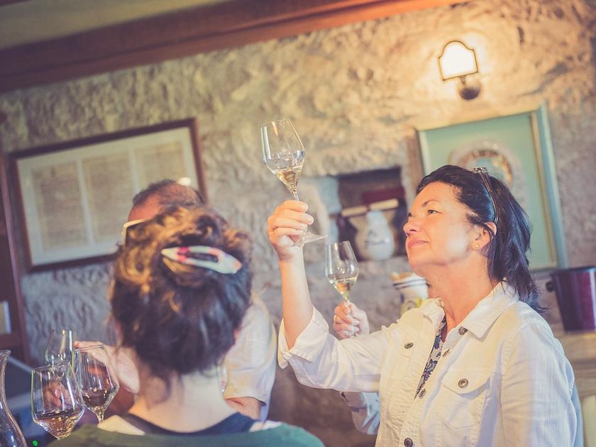 Guest in a stone tasting room holding a glass of white wine up to the light