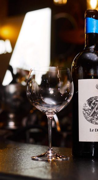 Bottle of Le Divine Malvazija Sur Lie with a cream woodcut label and blue capsule beside an empty glass on a dark bar
